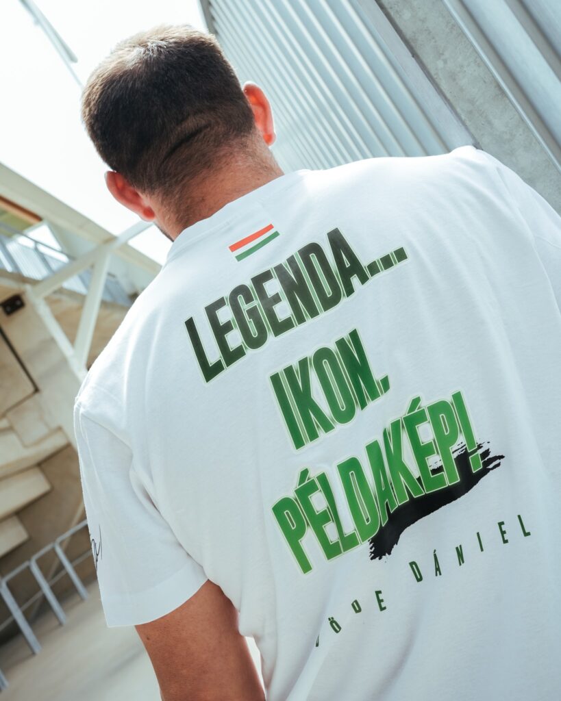 Böde Dániel hátulról, fehér pólóban, rajta a felirat: „Legenda… Ikon. Példakép!”