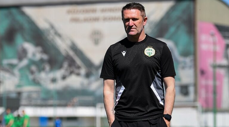 Robbie Keane edzés közben a Ferencváros játékosai előtt, háttérben klubmotívumos épületdekorációval.
