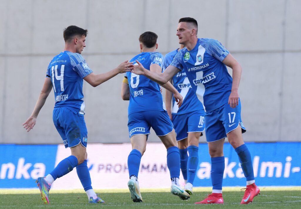 MTK-játékosok örülnek egy akció után a pályán, háttérben az FTC elleni meccs.